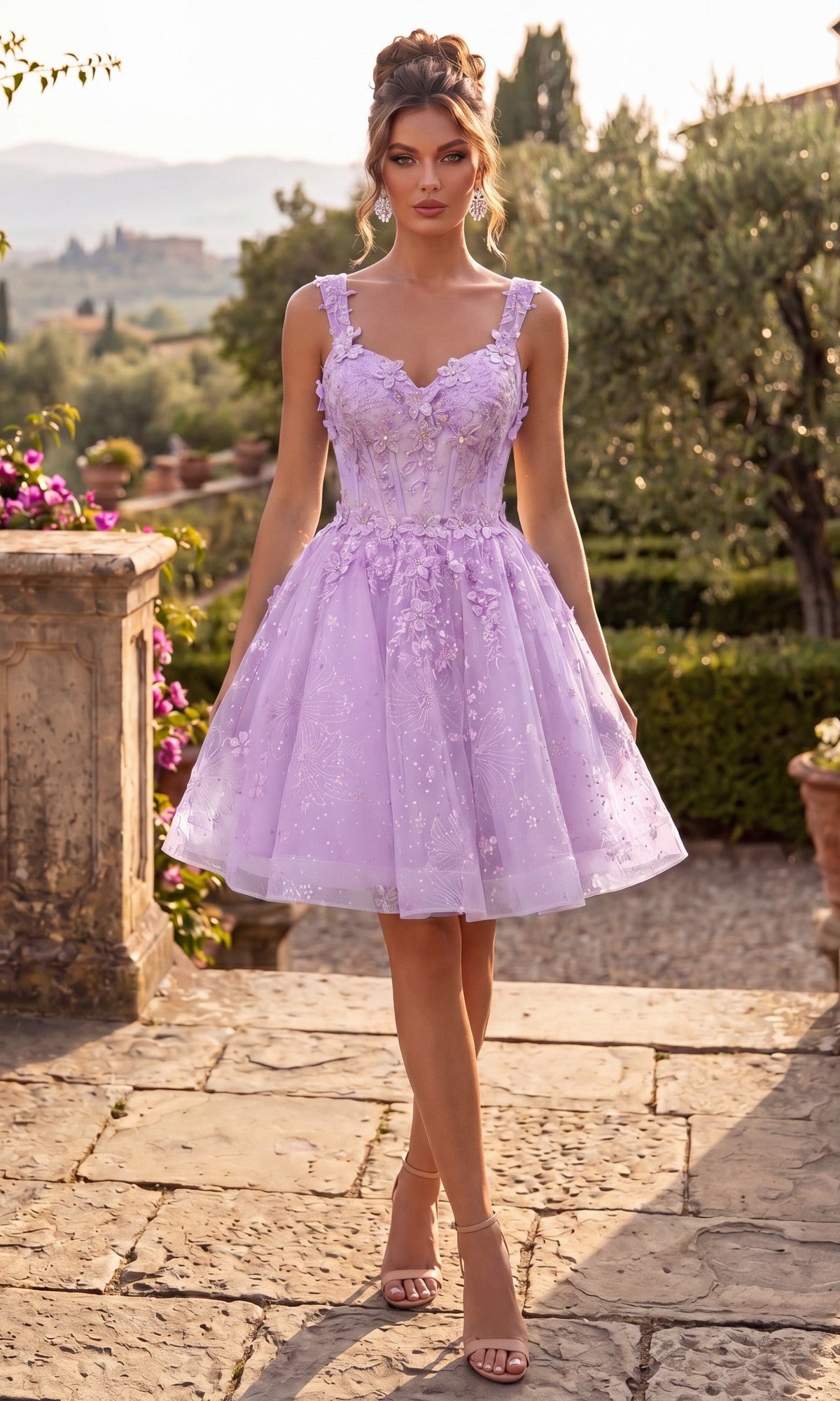 Wearing the Short Homecoming Dress: Chicas C372 in lavender, a woman stands outdoors framed by a stone patio, greenery, and flowers. The dress features delicate spaghetti straps, intricate lace floral embroidery, a flattering corset bodice, and a fit-and-flare silhouette. She pairs the look with nude heels.